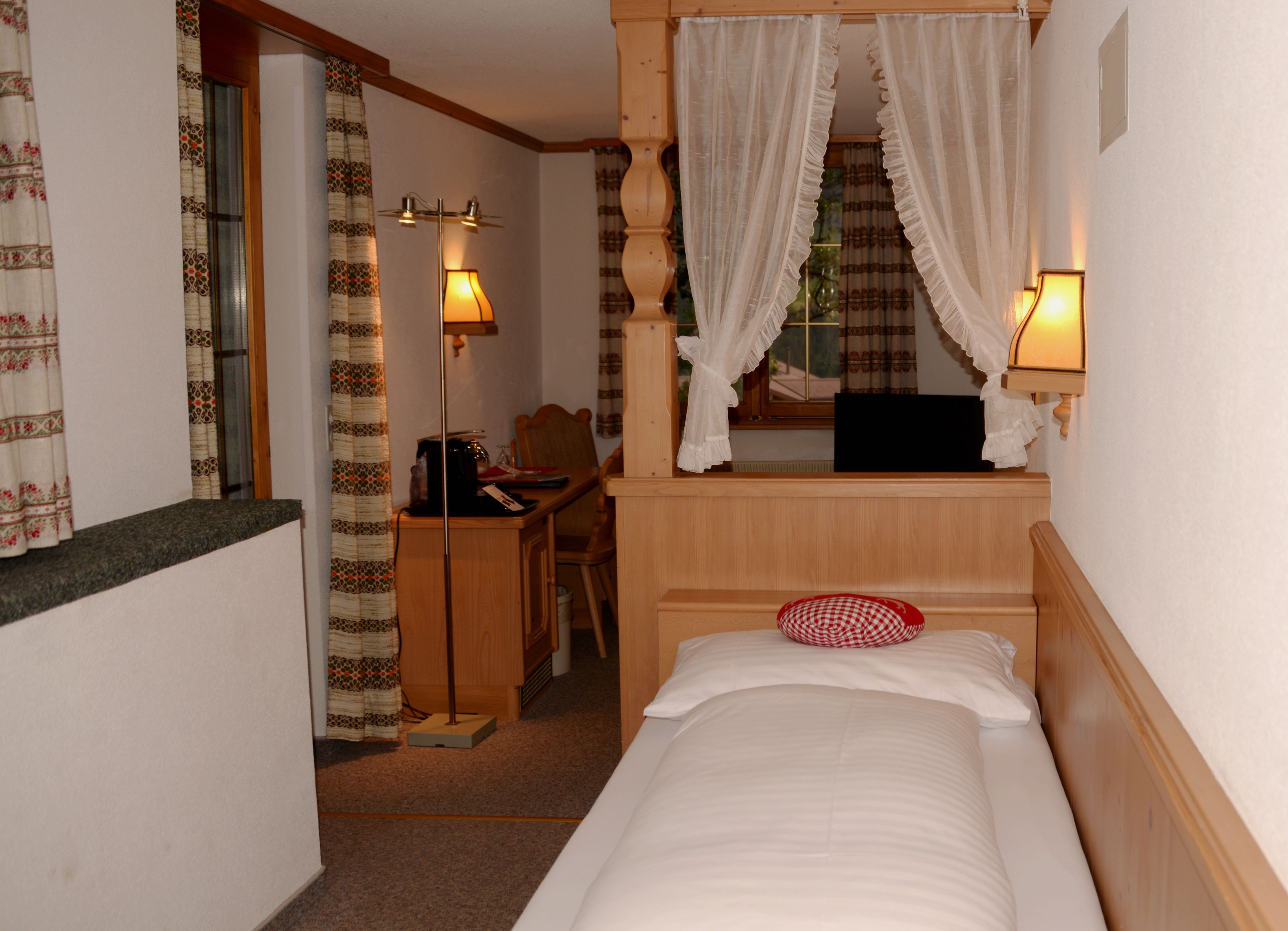 A bedroom with a bed, a desk, a chair, and a window with curtains.