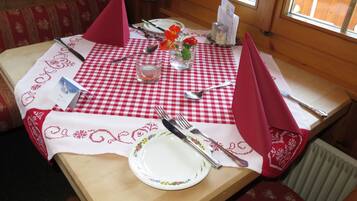 Een eettafel gedekt met een rood-wit geruit tafelkleed, een wit bord met bloemendecoraties, bestek, een kleine vaas met rode bloemen en een kandelaar.