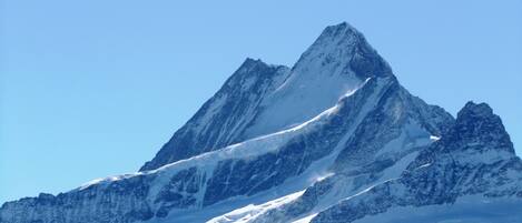 A snow-covered mountain peak with sharp, jagged peaks and a clear blue sky.