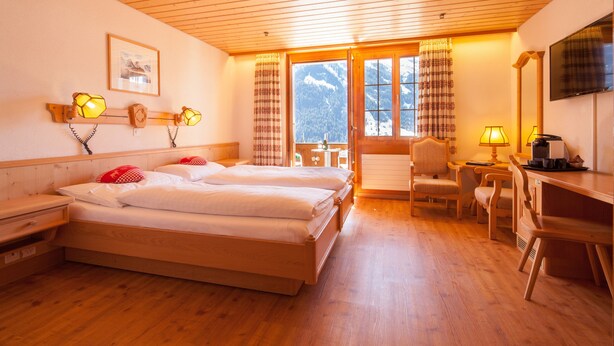 Habitación de hotel con pisos de madera, una cama, un escritorio, una silla y un televisor.