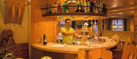 A bar area with wooden furniture, a variety of bottles, and a person serving.