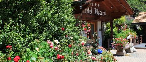 A wooden building with a sign reading "Hotel Mülbehof" surrounded by lush greenery and flowers.