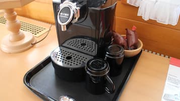 Una cafetera sobre una bandeja con una cuchara, una taza pequeña y un recipiente con cápsulas de café.