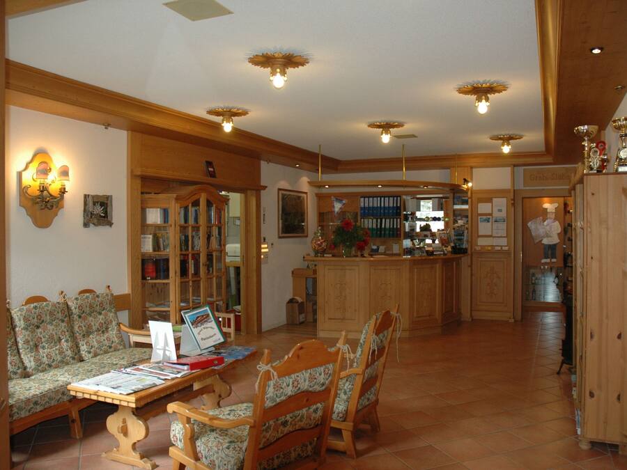 Amplia sala de estar con un sofá de madera, una mesa de centro con libros y una cocina al fondo.