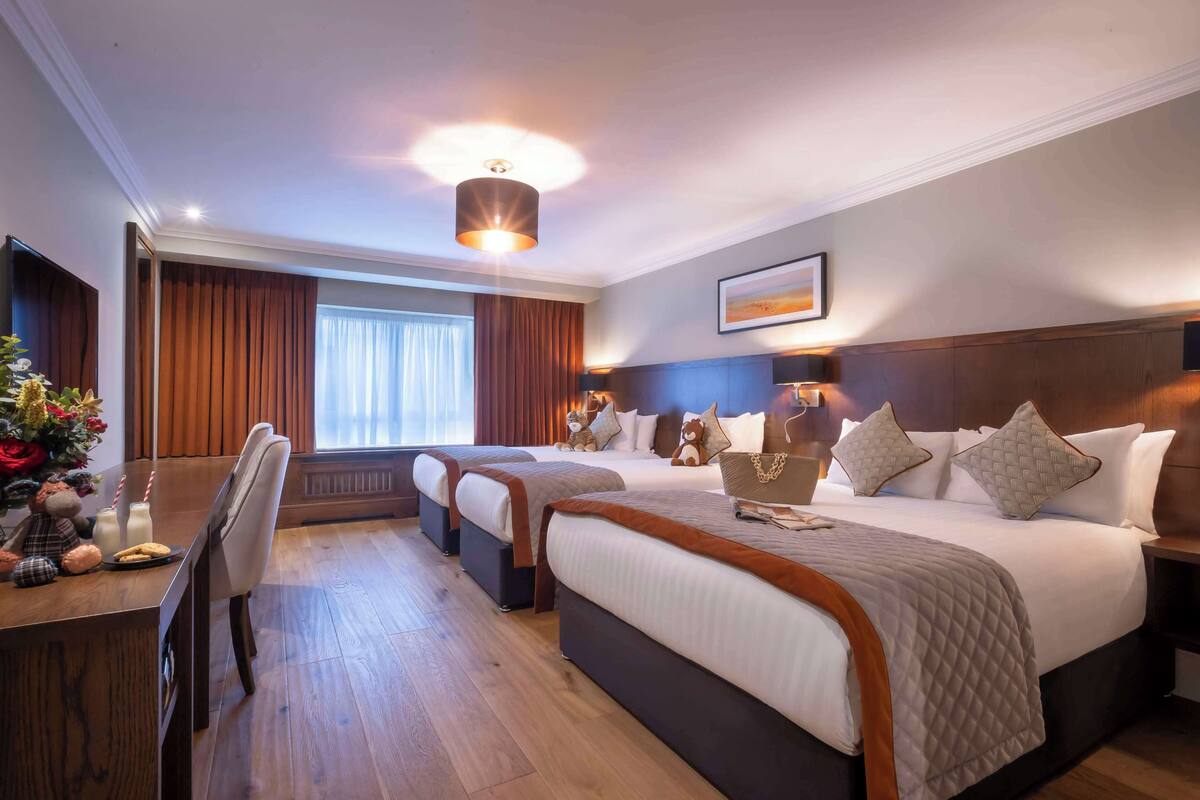 A hotel room with a large bed, a desk with a chair, and a window with curtains.