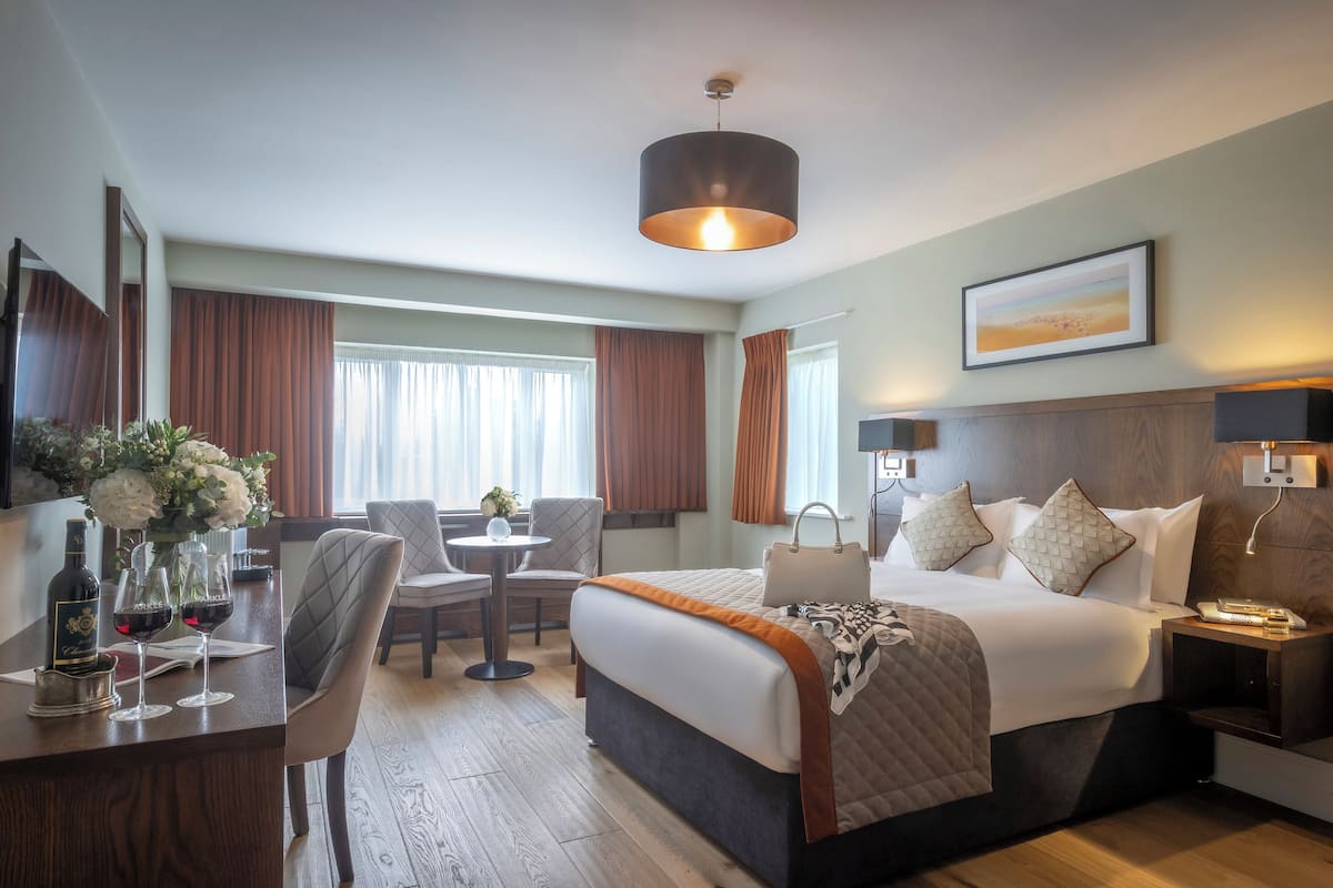 A hotel room with a bed, bedside table, lamp, and a view of the outdoors.