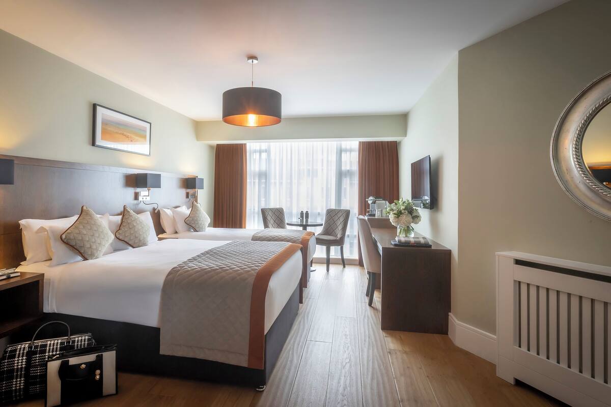 A hotel room with a large bed, bedside tables, a desk, a chair, a mirror, and a view of the outdoors.