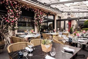 Een terras met tafels gedekt voor gasten, omringd door weelderige bloemstukken en rieten meubilair.