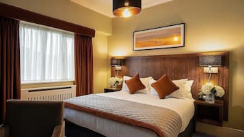 A hotel room with a large bed, two bedside tables with lamps, a chair, a window with curtains, and a framed picture on the wall.