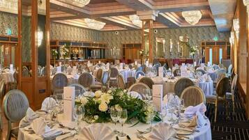 Une salle de banquet avec des tables rondes dressées pour un événement formel, agrémentée de compositions florales et d’une décoration de table élégante.