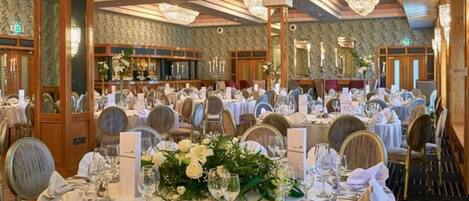 Un salón de banquetes con mesas redondas dispuestas para un evento formal, con centros de mesa florales y elegantes mantelería.