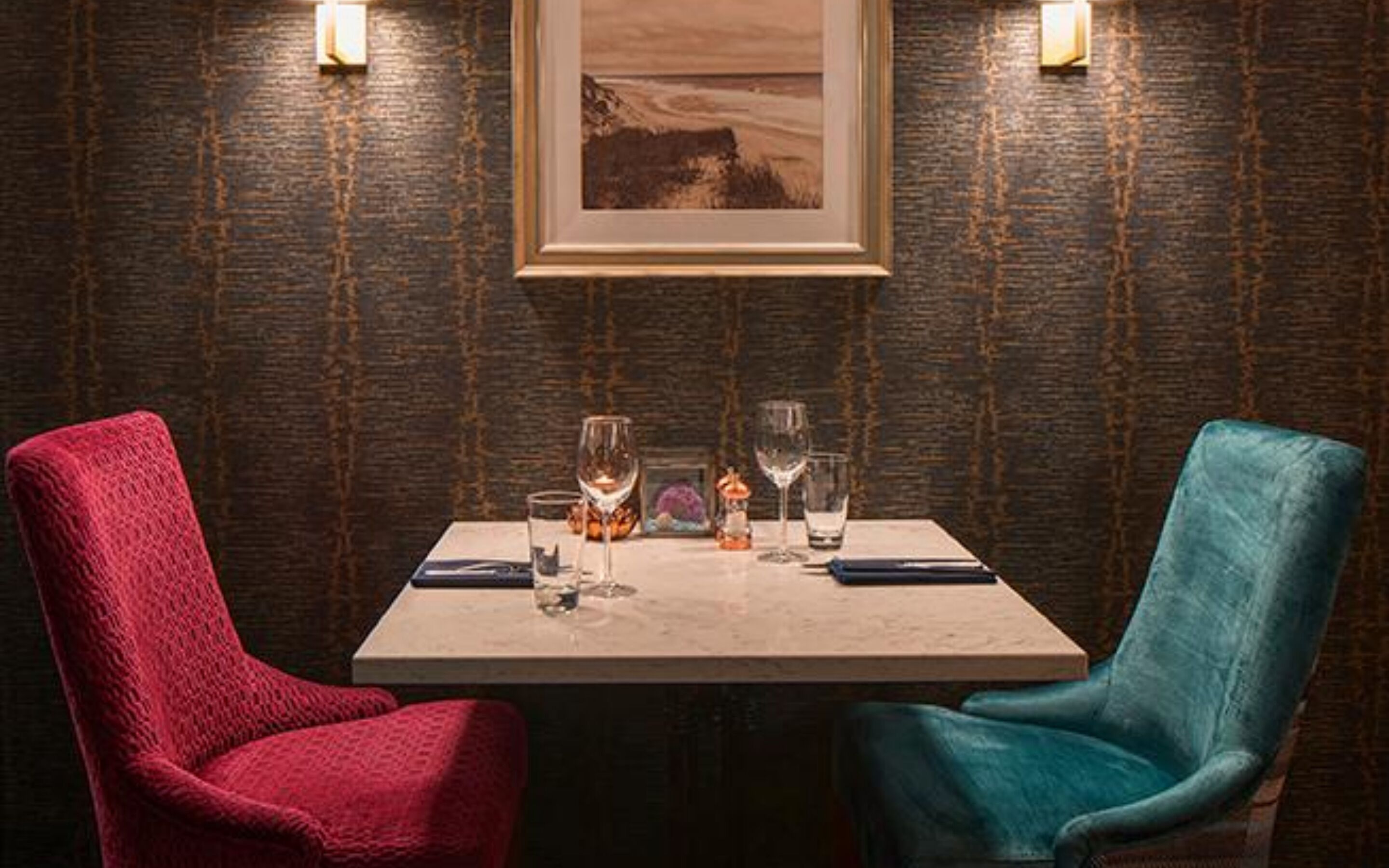 Een eettafel met twee stoelen, een lijst met een foto aan de muur en een structuurmuur.