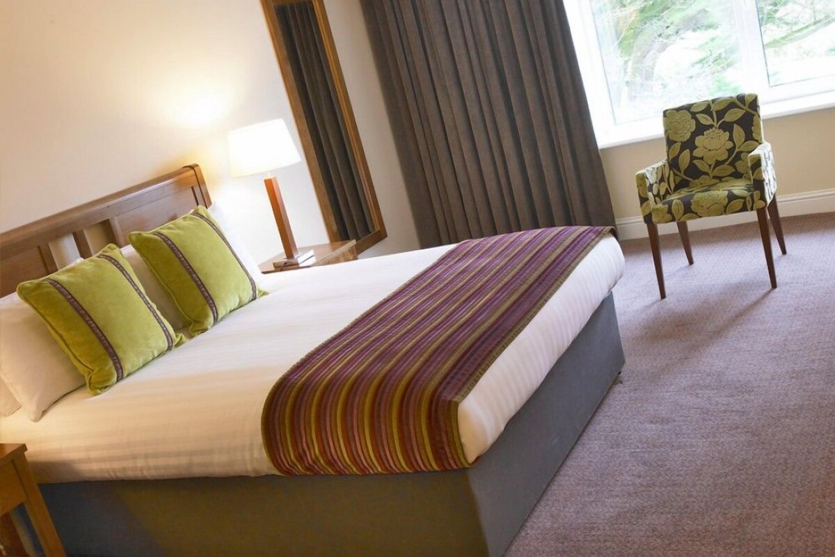 A hotel room with a bed, a chair, a lamp, and a window with curtains.