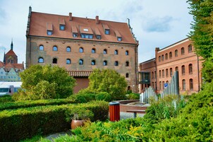 Ein historisches Gebäude mit einem Ziegeldach und zahlreichen Fenstern, umgeben von gepflegter Bepflanzung und einem Parkplatzschild.