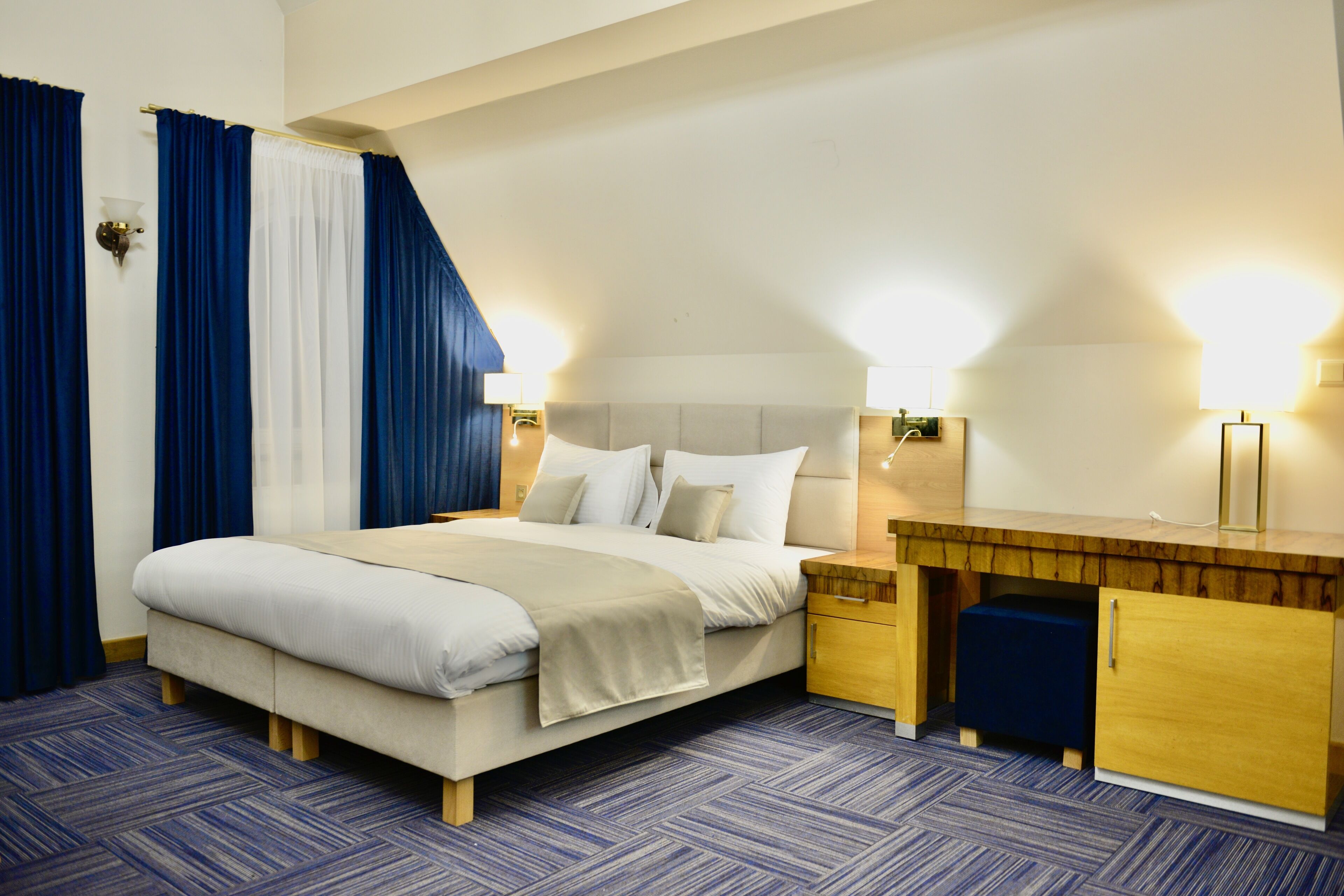 A hotel room with a bed, bedside tables, a desk, and a wardrobe.