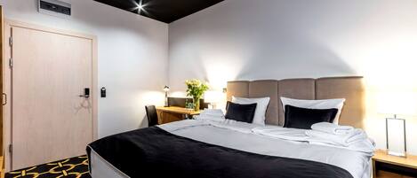 Una habitación de hotel con cama, mesita de noche, lámpara y escritorio con silla.