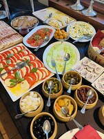 Un bufé con diversos alimentos, como tomates en rodajas, pepinos, aceitunas y queso.