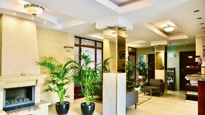 Un hall con chimenea, plantas en macetas, una zona de estar y un mostrador de recepción.