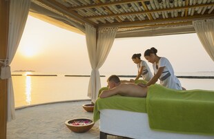 Sesión de masajes en la playa, con un toldo de madera y vistas al atardecer.