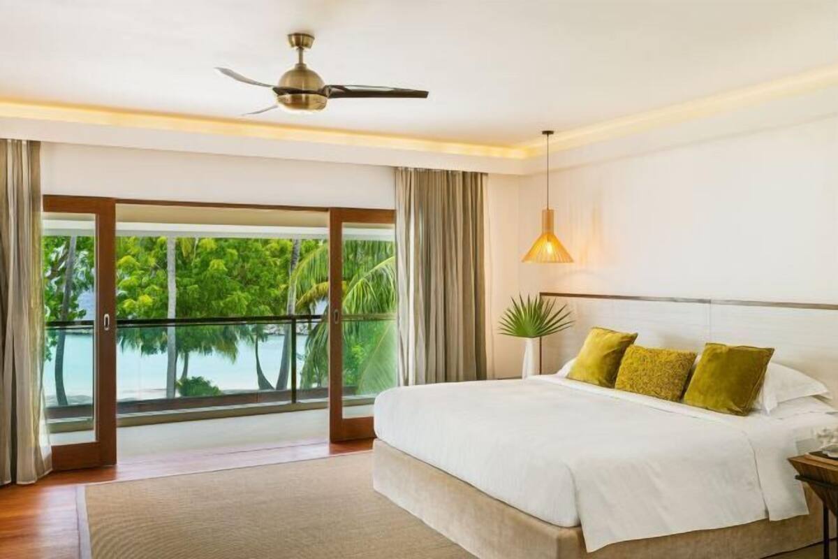 Una camera da letto con un letto, un ventilatore a soffitto, un'ampia finestra vista sul verde e un balcone.