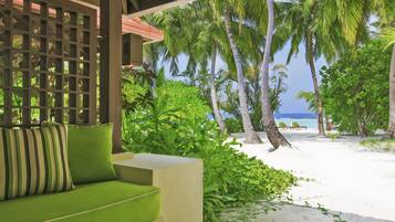 A covered outdoor seating area with a green sofa and a wooden lattice partition.