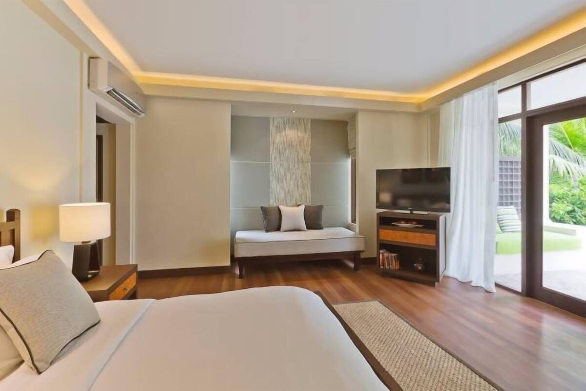 Una camera d'albergo con un letto, una TV, un divano e un'ampia finestra.