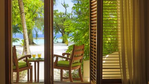 Una silla y una mesa de madera junto a una ventana con vistas a una playa y palmeras.