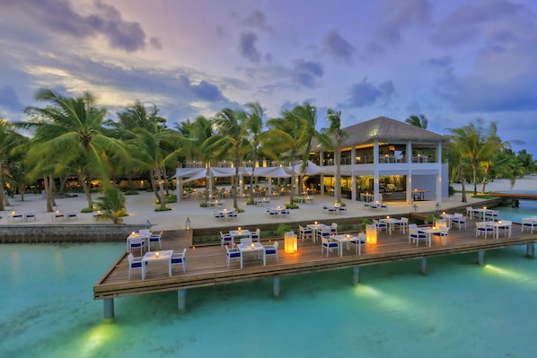 A resort with a poolside dining area, a wooden deck, and a building with a thatched roof.