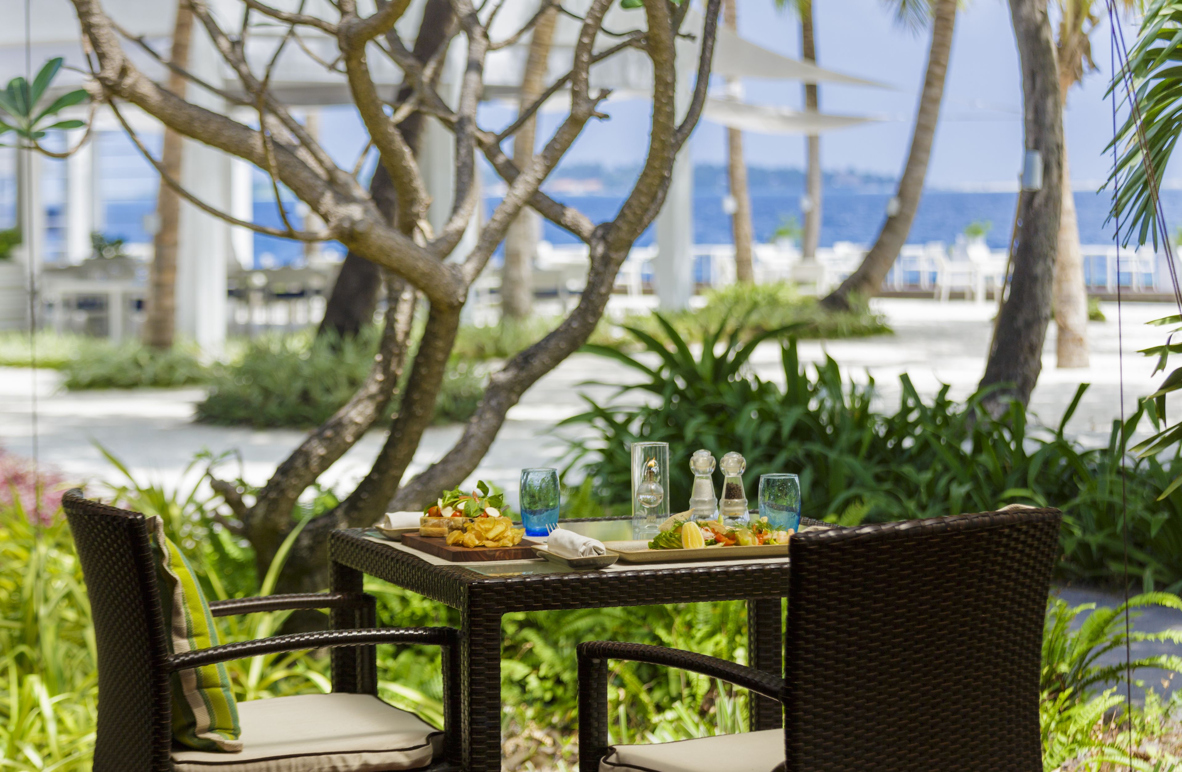 A dining table with wicker chairs and a view of the ocean.