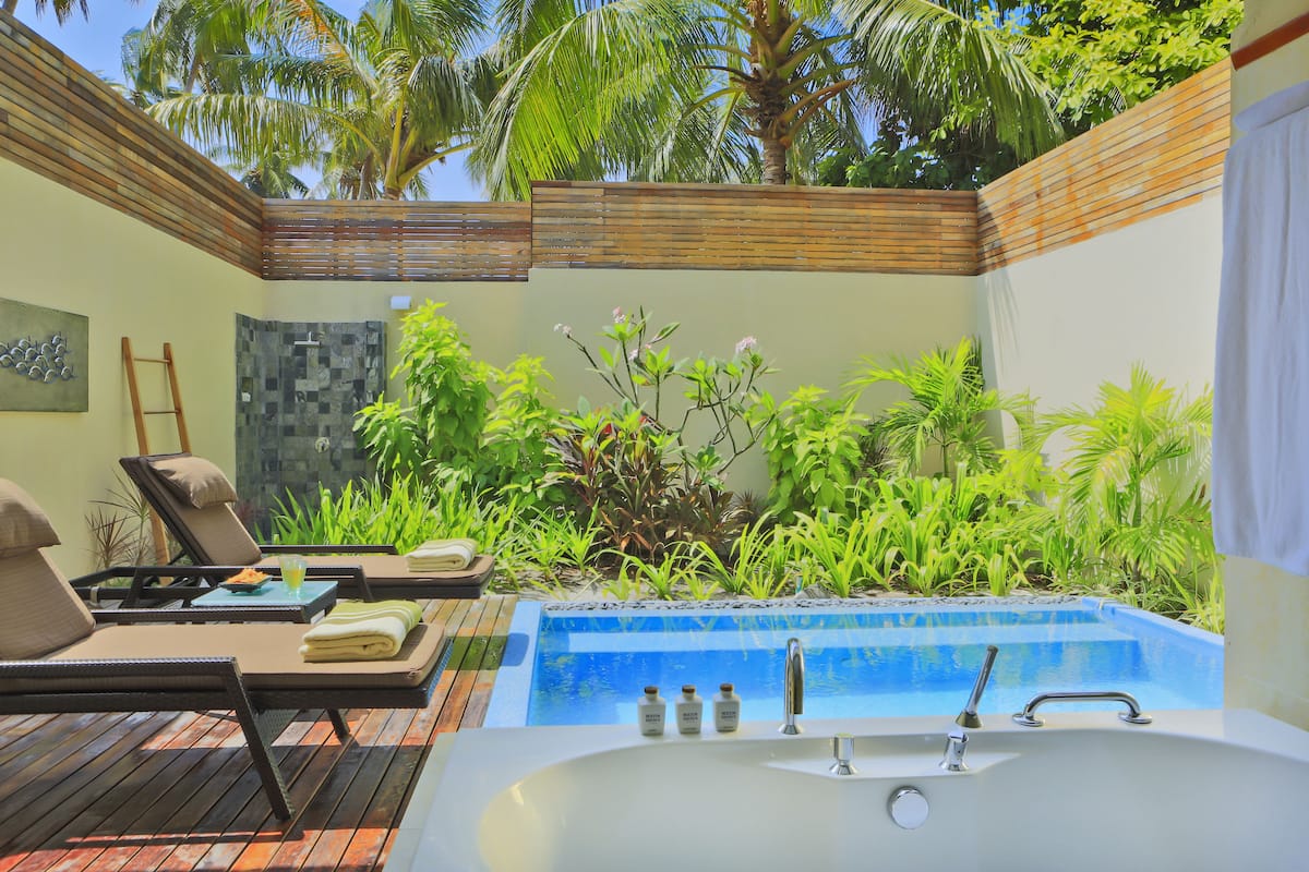 A pool area with lounge chairs, a hot tub, and a small waterfall feature.