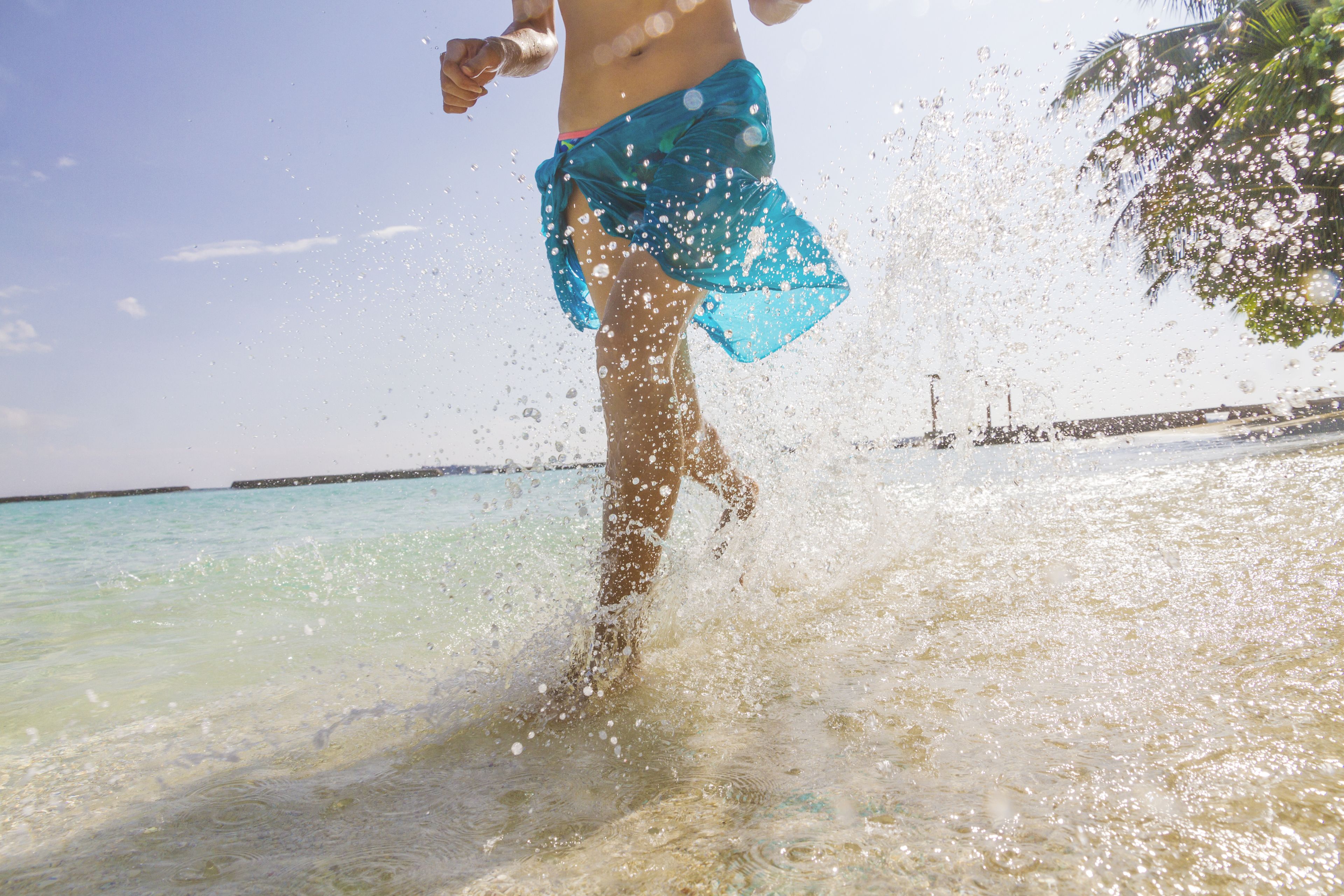 A person in a blue skirt standing in shallow water with splashes around them.
