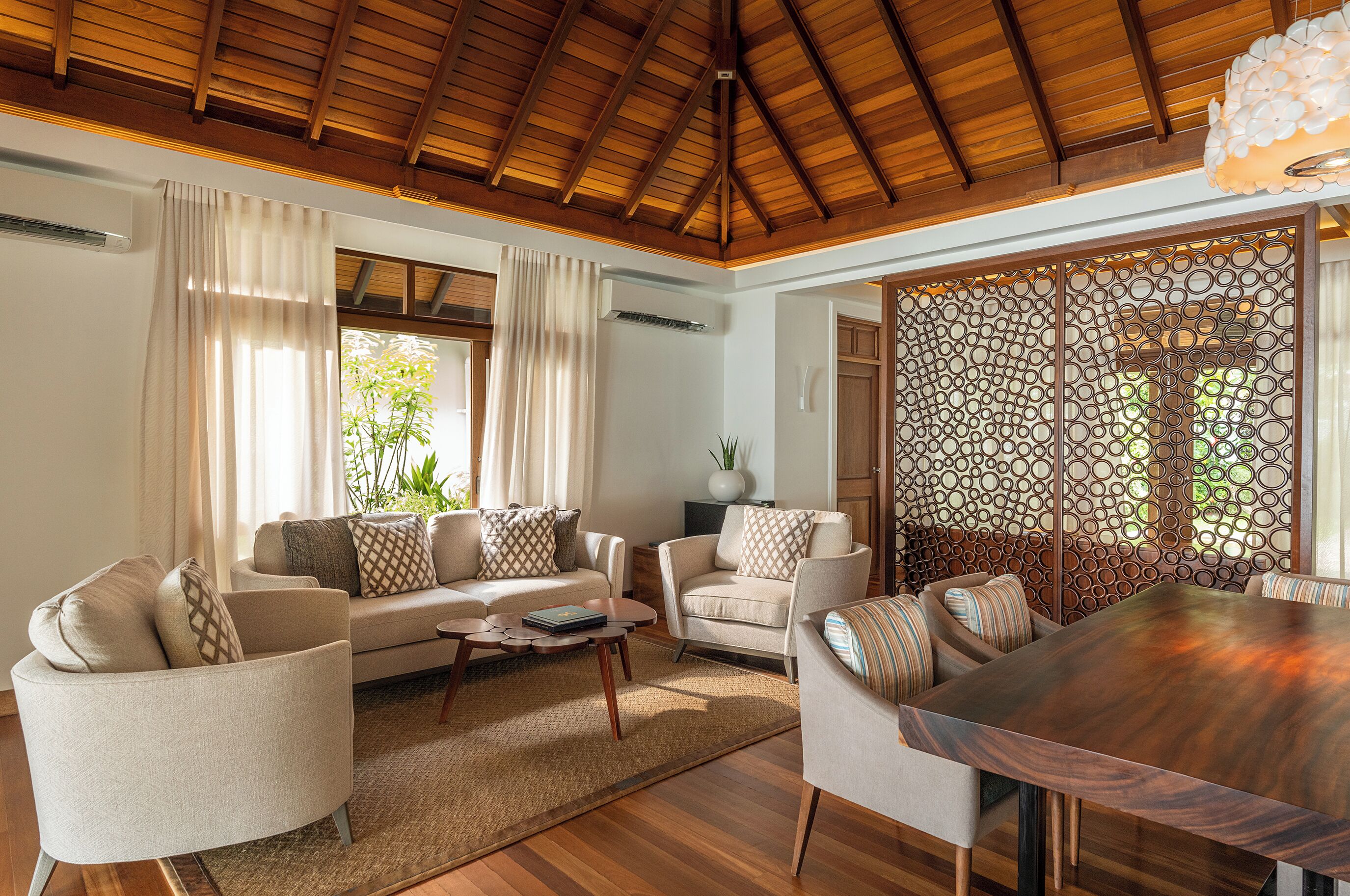 A spacious living room with a wooden ceiling, a large dining table, and comfortable seating.