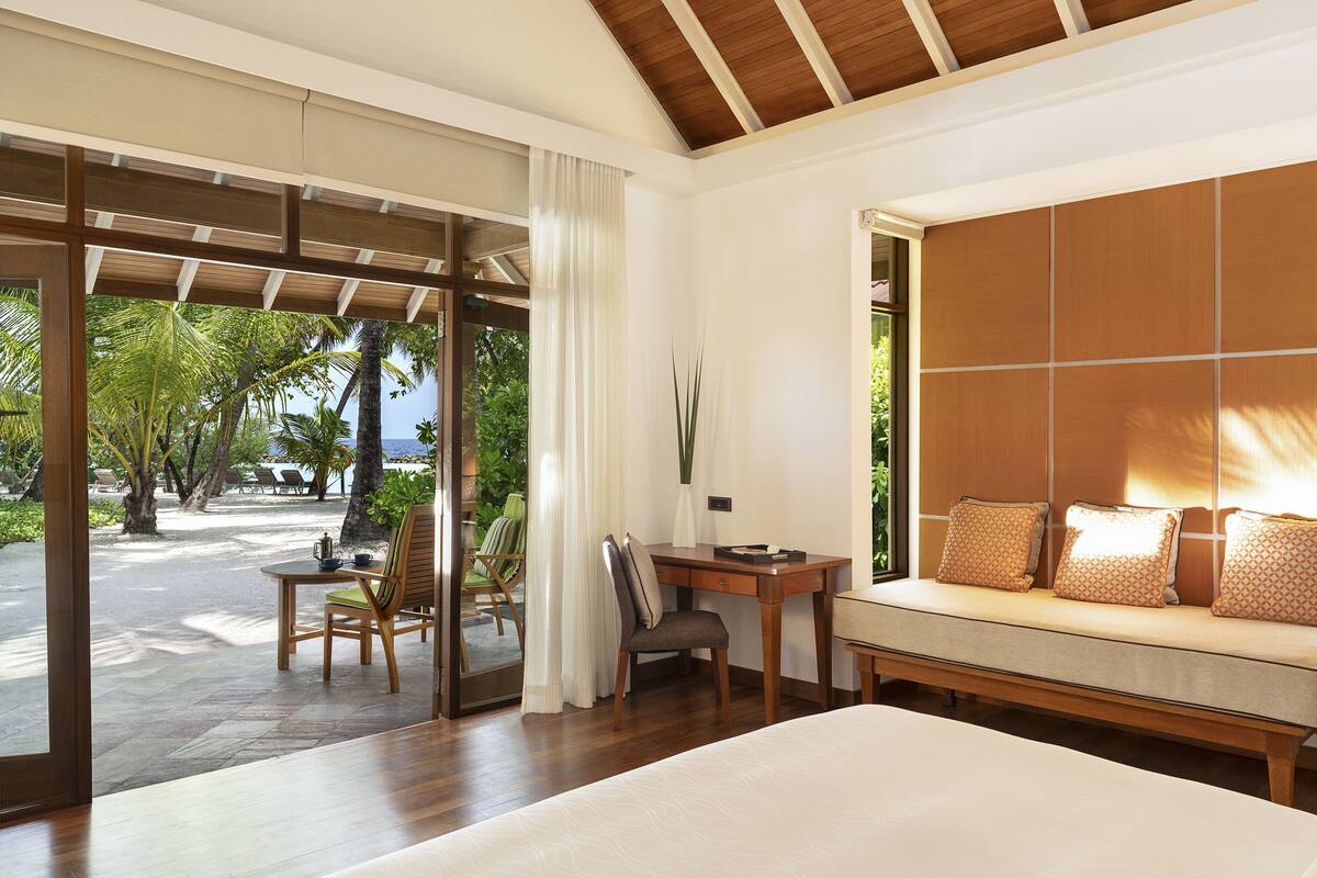 Una camera d'albergo con un letto, una scrivania, una sedia e vista su palme e l'oceano.