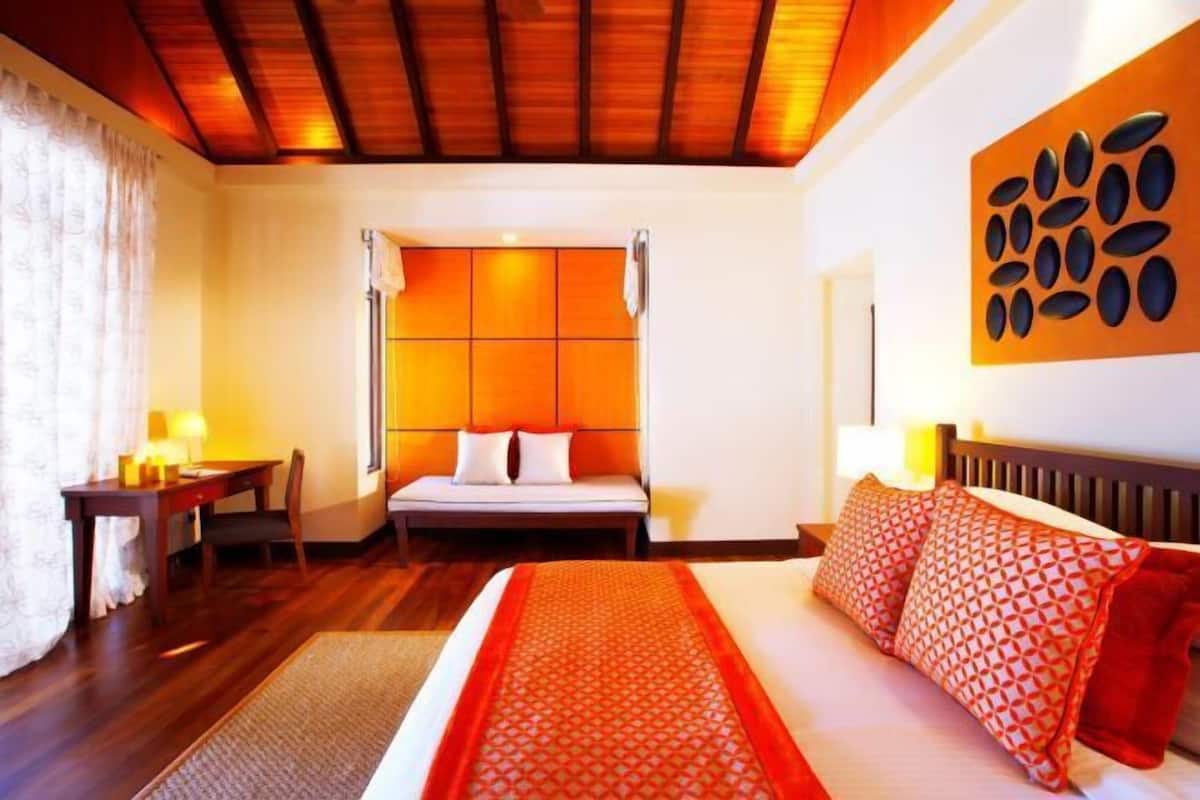Camera d'albergo con soffitto in legno, un letto con copriletto decorato, una scrivania con sedia e un'opera d'arte appesa al muro.