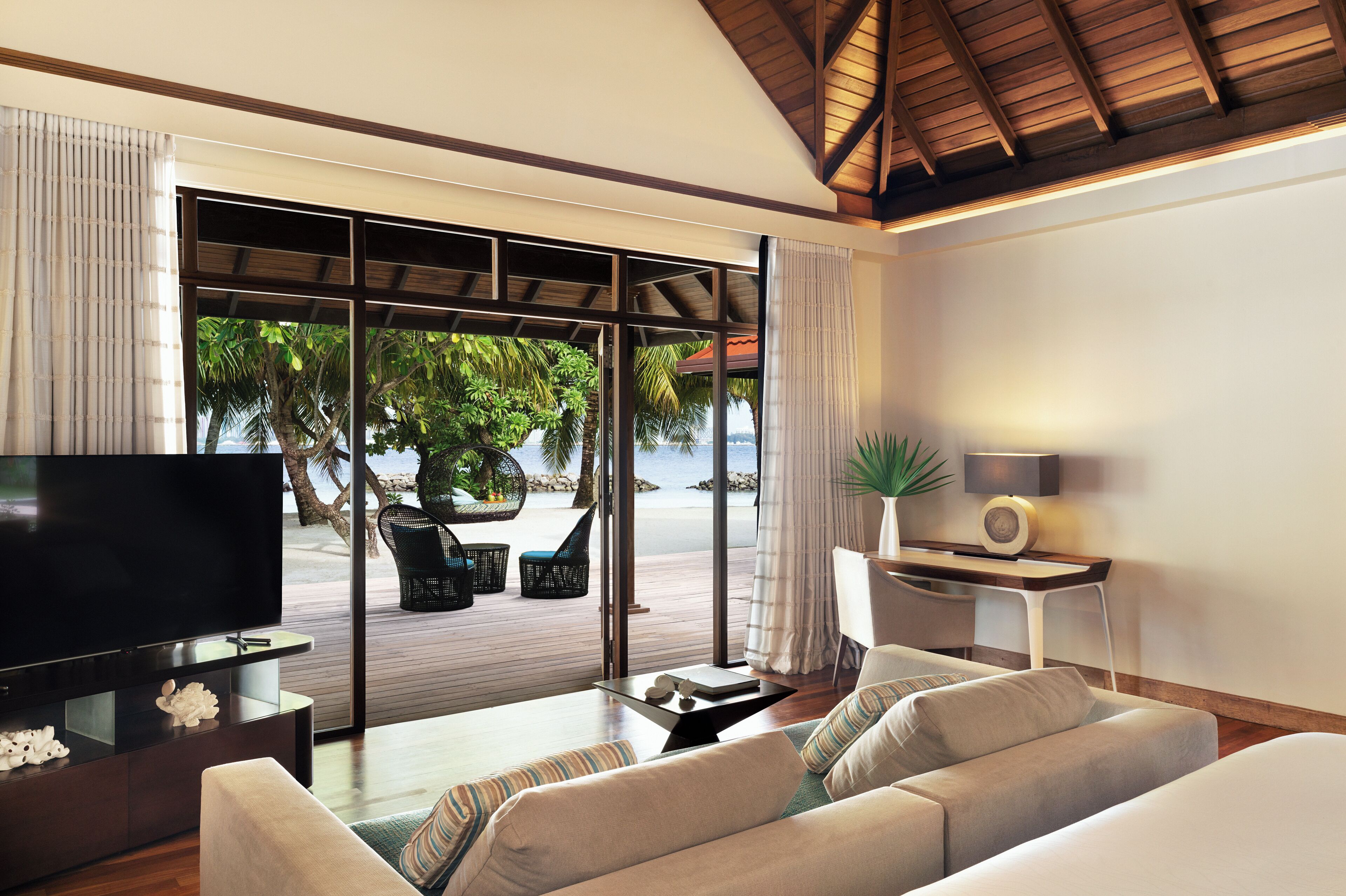 Una sala de estar moderna con televisor, sofá y vista a una playa tropical.