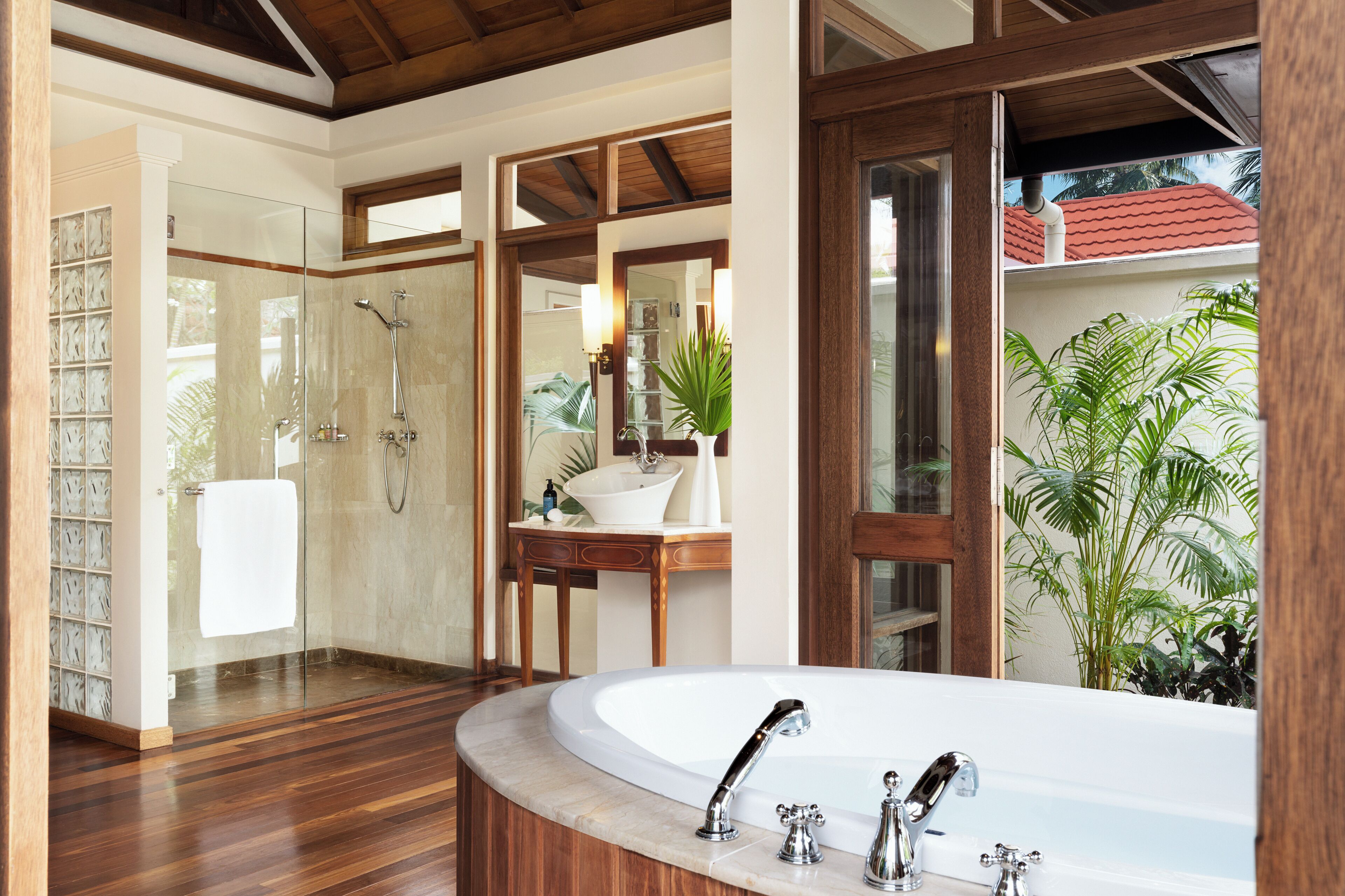 Un baño moderno con una bañera independiente grande, una ducha con mampara de vidrio y un tocador de madera con lavabo y espejo.
