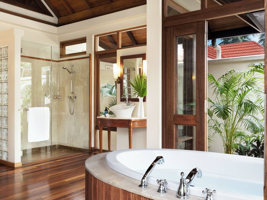 Un baño moderno con una bañera independiente grande, una ducha con mampara de vidrio y un tocador de madera con lavabo y espejo.