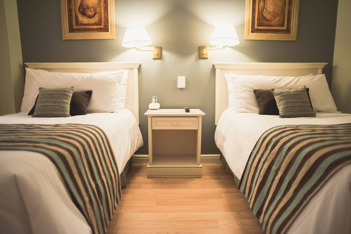 Ein Hotelzimmer mit zwei Betten, jeweils einem Nachttisch, einer Lampe und einem Bild an der Wand.