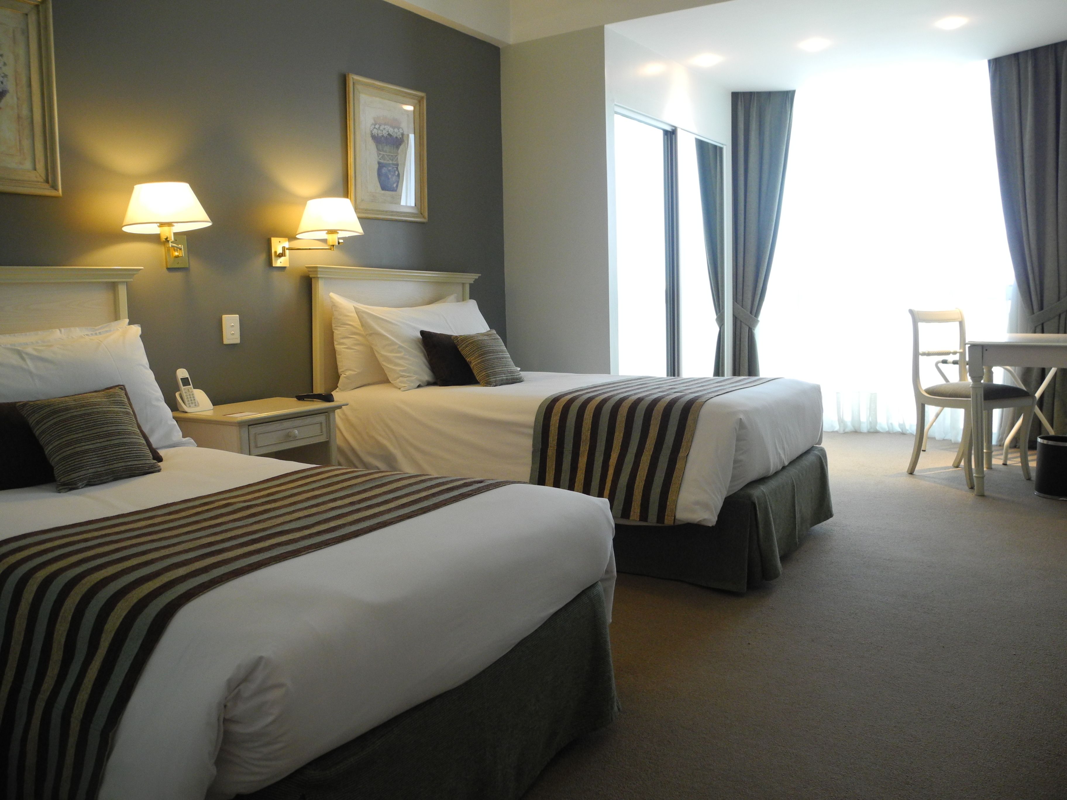 A hotel room with two beds, a desk, and a chair.