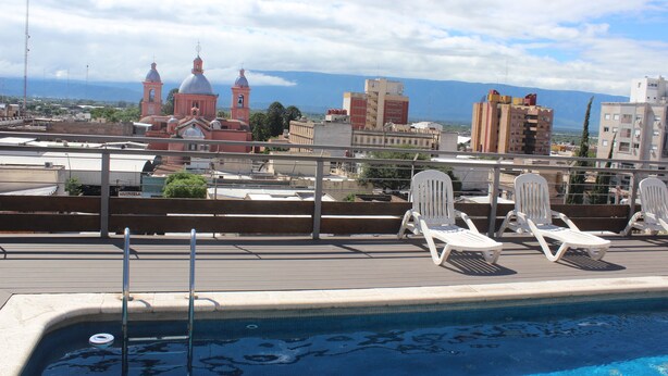 Piscina no terraço com espreguiçadeiras, vista para um horizonte urbano com edifícios históricos e céu claro.