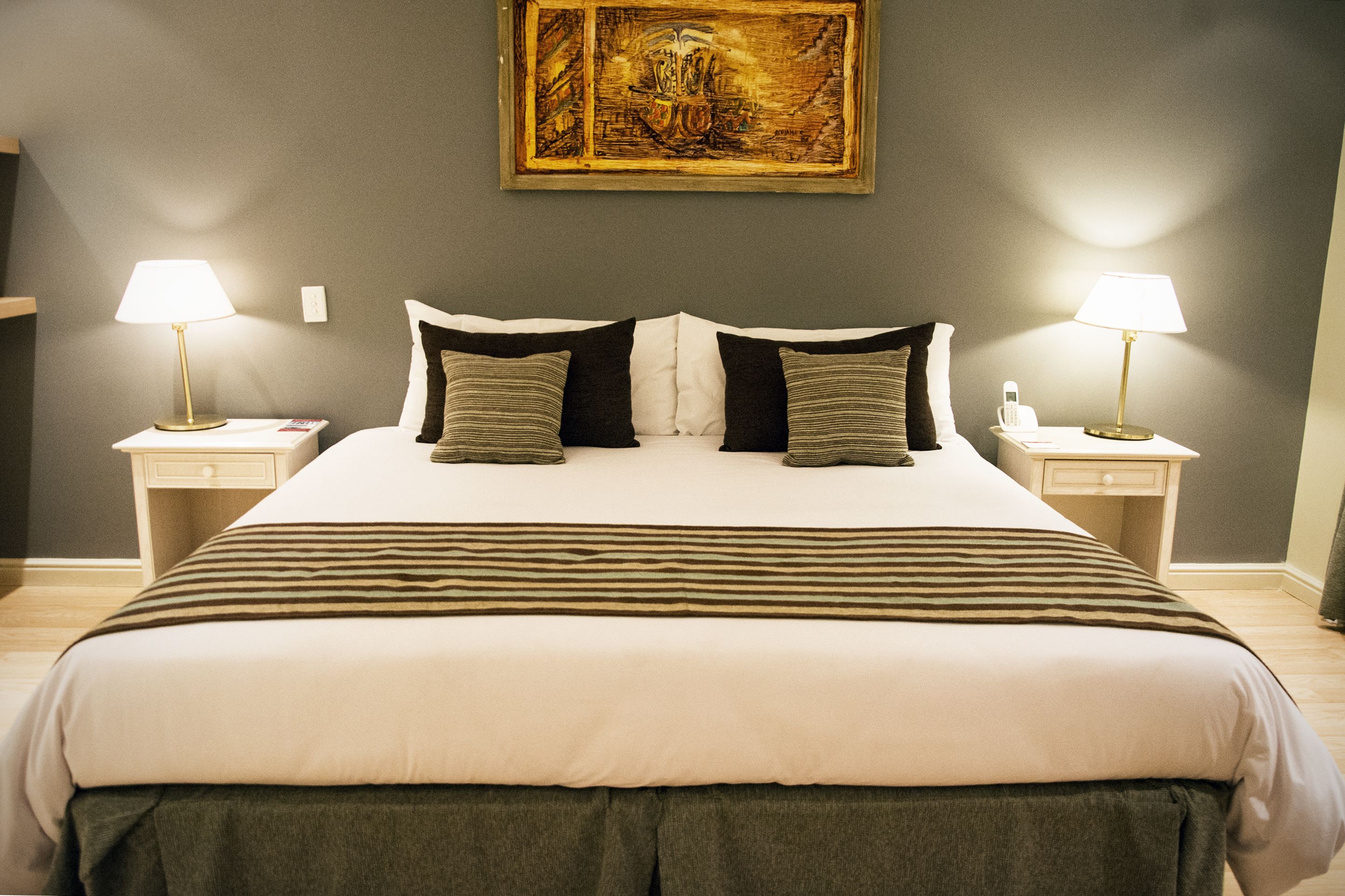 A neatly made bed with a striped bedspread, two bedside lamps, and a painting on the wall.