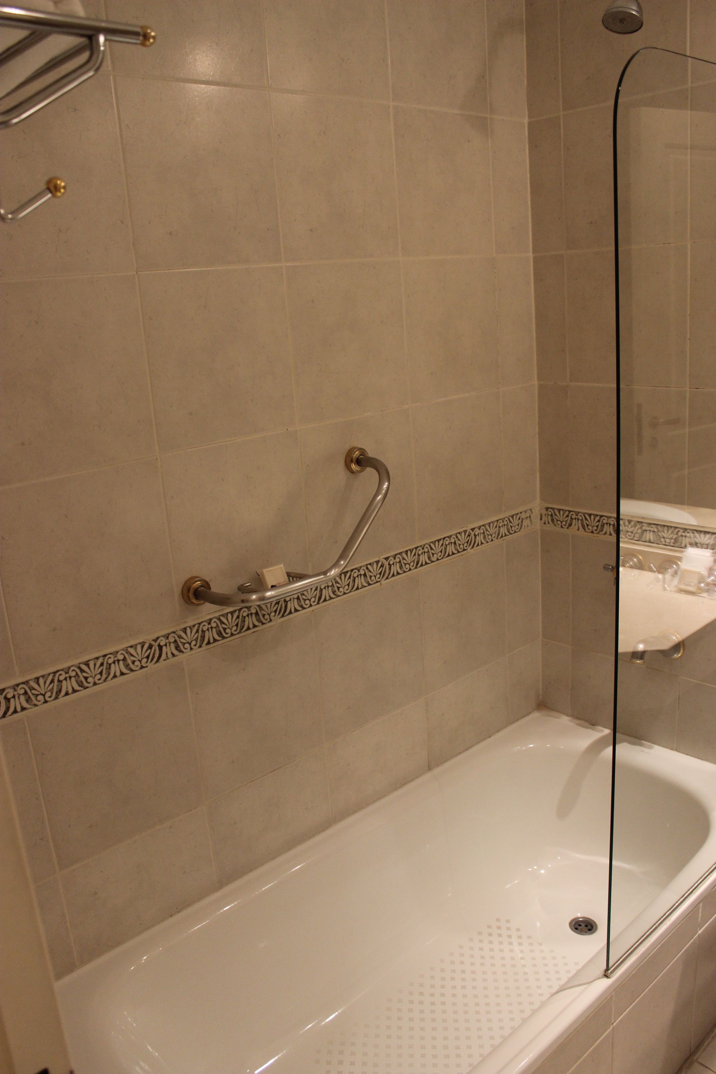 A bathroom with a bathtub, a shower, and a handrail.