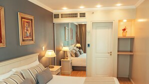 Quarto de hotel com cama, duas mesas de cabeceira com luminárias, uma porta que dá para outro quarto e uma estante com um vaso.
