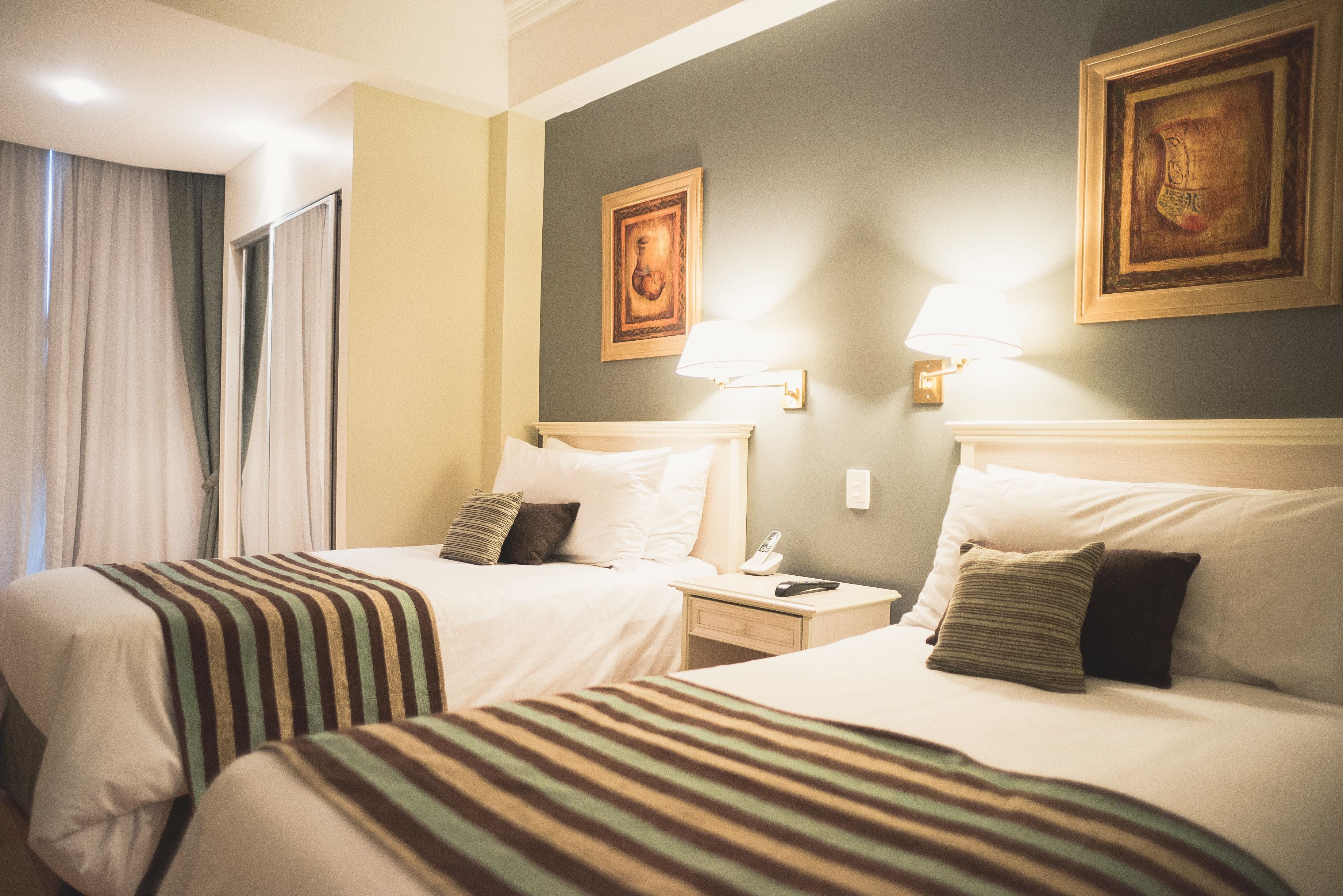 A hotel room with two beds, a nightstand with a lamp, and a painting on the wall.