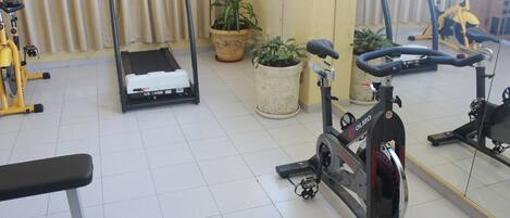 Un gimnasio con equipo de ejercicio, incluyendo cintas de correr y una bicicleta estática, además de un banco.