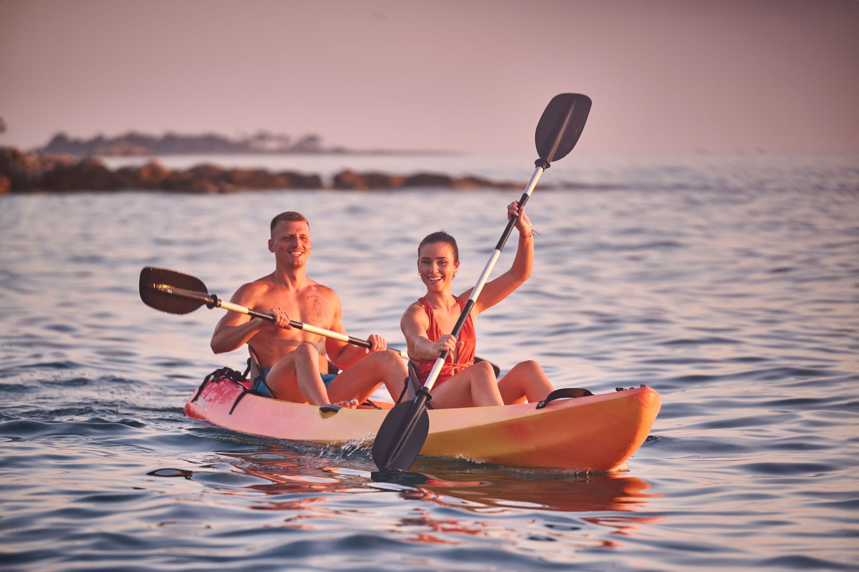 Dos personas en kayak sobre aguas tranquilas durante el atardecer.