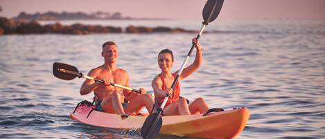 Two people kayaking on a calm body of water during sunset.