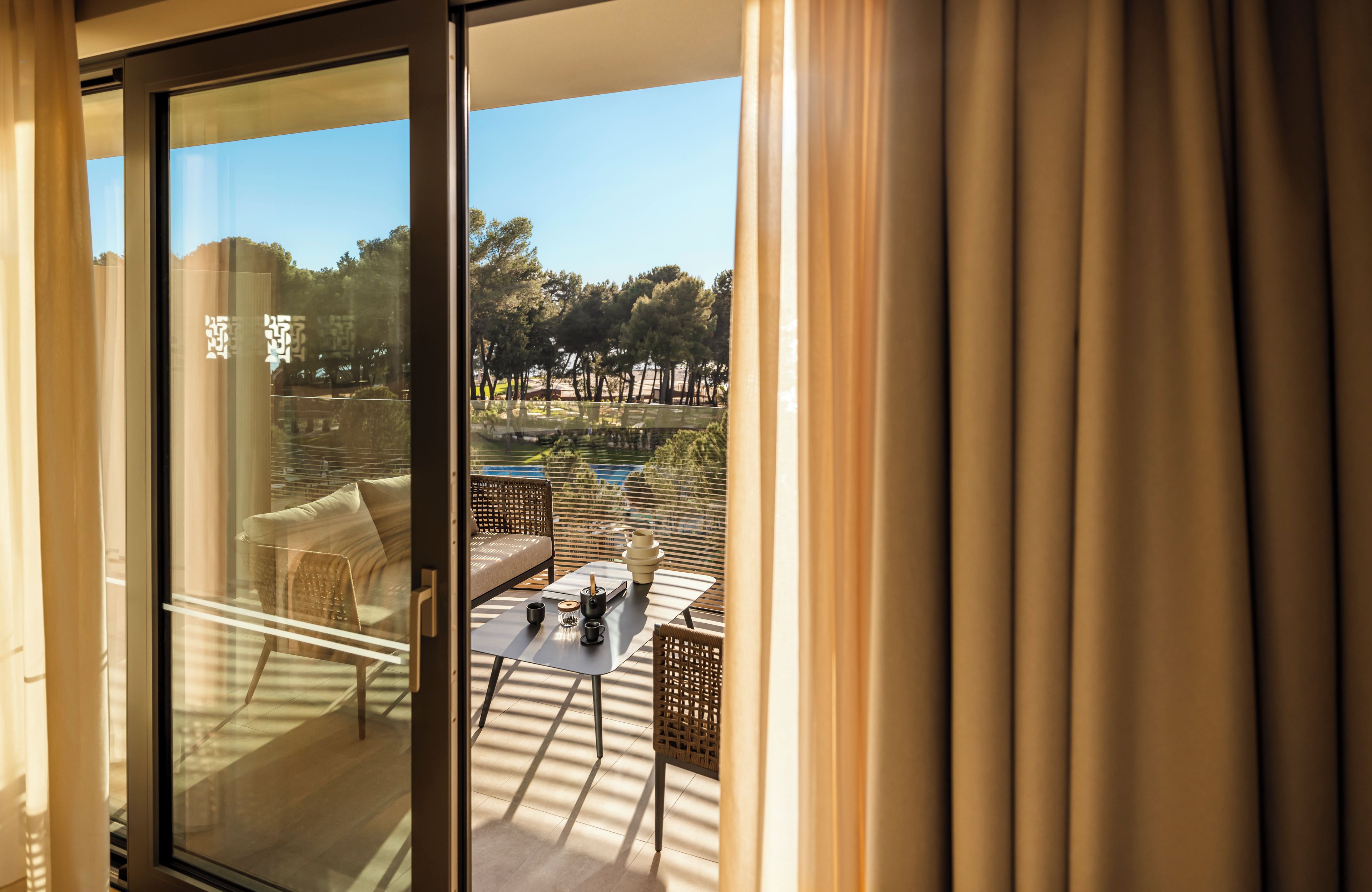 A room with a glass door leading to an outdoor seating area with a table, chairs, and a view of a garden.