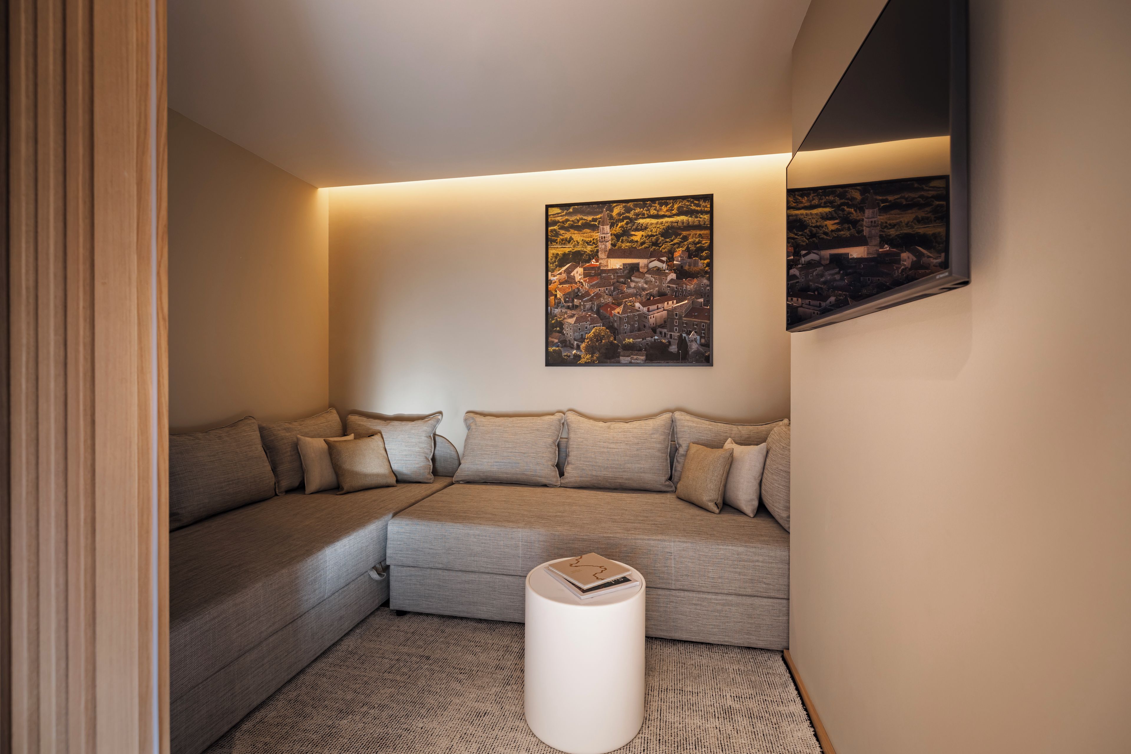 A modern living room with a sectional sofa, a white side table, and a framed landscape painting on the wall.