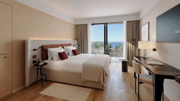 A modern hotel room with a large bed, a desk, and a view of the sea.